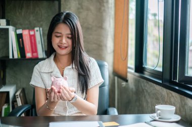 Gülümseyen kadın kumbarasını elinde tutuyor, birikimleri ve finansal planlamaları simgeliyor..