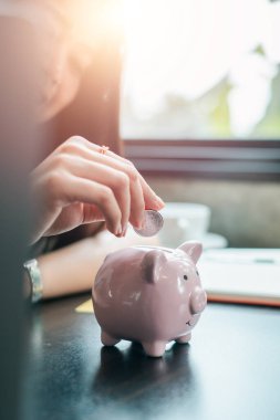 Birikimleri ve finansal planlamaları simgeleyen pembe kumbaraya para sokan bir kadının yakın plan çekimi..