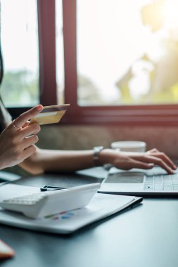 Parlak ve modern bir ortamda online alışveriş için kredi kartı ve laptop kullanan bir kadının yakın çekimi..