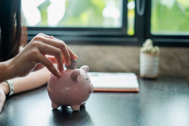 Birikimleri ve finansal planlamaları sembolize eden pembe bir kumbara içine bozuk para koyan bir kadının yakın çekimi..