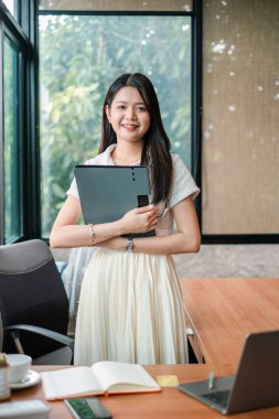 Profesyonel bir kadın elinde tabletle parlak bir ofiste duruyor, toplantıya ya da sunuma hazır..