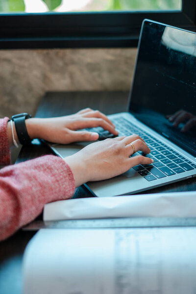 Hands typing on a laptop in a well-lit workspace, creating a productive and cozy atmosphere.
