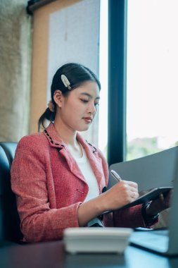 Çağdaş ofis ortamında dijital tablet kullanan kırmızı ceketli bir kadın..
