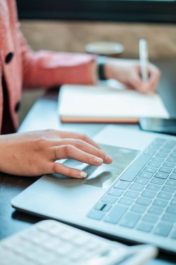 Bir insanın dizüstü bilgisayar kullanarak ve notlar yazarak, üretkenliği ve modern çalışma ortamlarını sembolize ederek yakınlaşması.