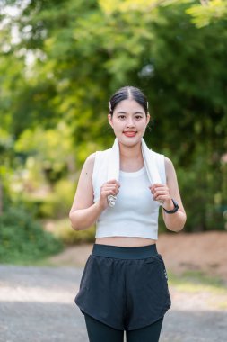 Spor giyimli genç bir kadın yeşil bir parkta koşuyor, spor salonu spor salonu ve sağlıklı bir yaşam tarzı sergiliyor..