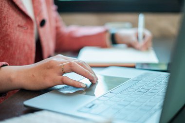 Bir dizüstü bilgisayar üzerinde çalışan, notlar yazan, üretkenliği ve modern ofis çalışmalarını sergileyen bir profesyonelin yakın çekimi..