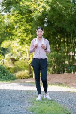 Spor elbiseli bir kadın yeşil, somut spor ve açık hava yaşam tarzıyla çevrili bir yolda kendinden emin bir şekilde duruyor..