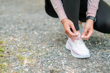 Beyaz koşu ayakkabılarını çakıllı bir yolda bağlayan birinin yakın çekimi. Açık havada egzersize hazır..