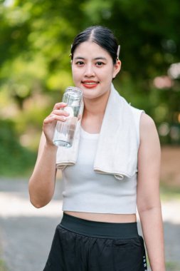 Sporcu genç bir kadın açık havada içme suyu içiyor. Sağlıklı yaşam tarzını ve su ihtiyacını karşılıyor..