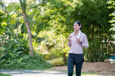 Havlu giymiş bir kadın yeşil park ortamında ferahlatıcı bir yürüyüşün tadını çıkarıyor..