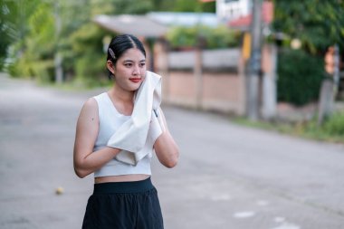 Spor kıyafetli genç bir kadın banliyö mahallesinde egzersiz yaptıktan sonra serinlemek için havlu kullanıyor..