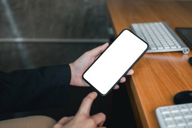 Profesyonel, ahşap ofis masasında boş ekranlı akıllı telefon tutuyor. Uygulama ya da web sitesi modeli için ideal..