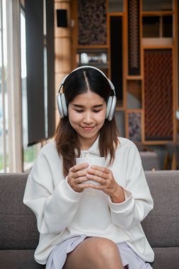 Kahveden zevk alan gülümseyen bir kadın şık bir kafede kulaklıkla müzik dinliyor..