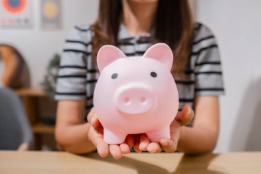 Modern bir ortamda tasarruf ve finansal planlamayı temsil eden pembe domuz kumbarası tutan bir kadının yakın çekimi..