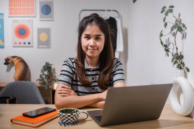 Genç bir kadın, dizüstü bilgisayarı olan bir masada oturuyor, modern dekorlarla çevrili, profesyonel bir iş ortamını somutlaştırıyor..