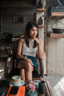 Kırsal dekorlu şık bir kafede oturan bir kadın huzurlu bir anın tadını çıkarıyor. Doğal ışık içeri akıyor, sıcak atmosferi vurguluyor.