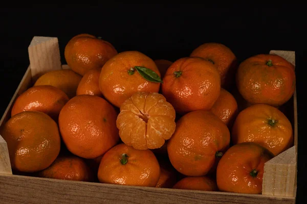 Orange tangerines in a wooden box on a black background. Tangerine with green leaf