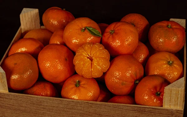 Orange tangerines in a wooden box on a black background. Tangerine with green leaf