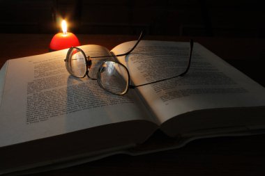 Açık bir kitap ve gözlük, mum ışığında.