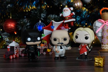 Funko Pop action figures of DC comics heroes Batman, The Penguin and Harley Quinn. Christmas tree with ornaments, small wooden train, festive decor. clipart