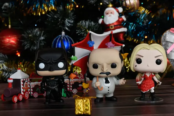 DC çizgi roman kahramanları Batman, Penguen ve Harley Quinn 'in aksiyon figürleri. Süslü Noel ağacı, küçük ahşap tren, şenlikli dekor..