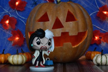 101 Dalmaçyalı animasyon filmindeki kötü karakter Cruella de Vil 'in Funko Pop aksiyon figürü. Cadılar Bayramı, Jack o fener, balkabağı, yapraklar çelenk ışığı.