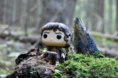 Funko Pop action figure of hobbit Frodo with sword from fantasy movie The Lord of the Rings. Fabulous dense forest, green moss, large fallen tree. clipart