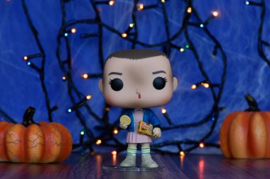 Televizyon dizisi Stranger Things 'den Eggo waffle ile Onbir' in Funko Pop aksiyon figürü. Mavi sisli arka plan, örümcek ağı, renkli ışıklar, Cadılar Bayramı balkabakları.