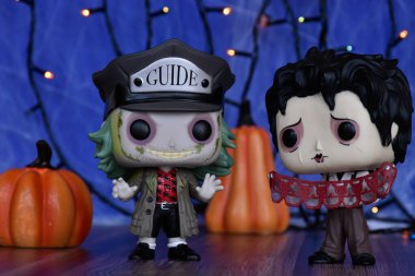 Funko Pop action figures of Beetlejuice and Edward Scissorhands from Tim Burton dark fantasy films. Blue fog background, colorful lights, Halloween pumpkins. clipart