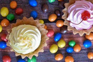 Renkli turtalar, protein kremalı kekler, ahşap masada çok renkli Dragee şekerler. Muz ve kiraz aromalı lezzetli bir tatlı, kısa hamurlu pasta. Parti yemeği. Üst görünüm.