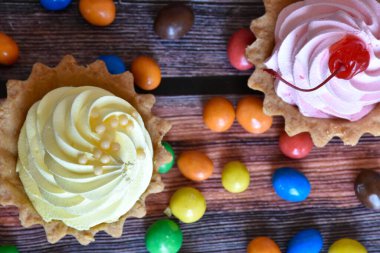 Renkli turtalar, protein kremalı kekler, ahşap masada çok renkli Dragee şekerler. Muz ve kiraz aromalı lezzetli bir tatlı, kısa hamurlu pasta. Parti yemeği. Üst görünüm.