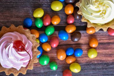 Renkli turtalar, protein kremalı kekler, ahşap masada çok renkli Dragee şekerler. Kiraz ve muz aromalı lezzetli bir tatlı, kısa hamurlu pasta. Parti yemeği. Üst görünüm.