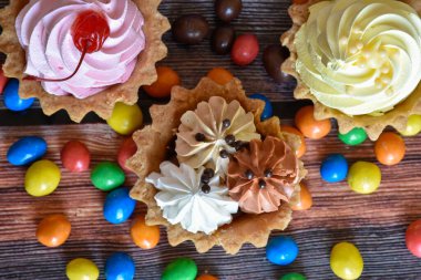 Renkli turtalar, protein kremalı kekler, ahşap masada çok renkli Dragee şekerler. Kirazlı, çikolatalı ve muzlu lezzetli bir tatlı, kısa hamurlu pasta. Parti yemeği. Üst görünüm.