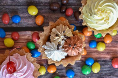 Renkli turtalar, protein kremalı kekler, ahşap masada çok renkli Dragee şekerler. Kirazlı, çikolatalı ve muzlu lezzetli bir tatlı, kısa hamurlu pasta. Parti yemeği. Üst görünüm.