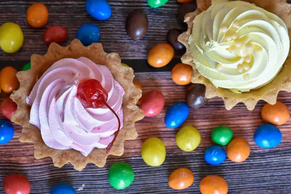 Renkli turtalar, protein kremalı kekler, ahşap masada çok renkli Dragee şekerler. Kiraz ve muz aromalı lezzetli bir tatlı, kısa hamurlu pasta. Parti yemeği. Üst görünüm.