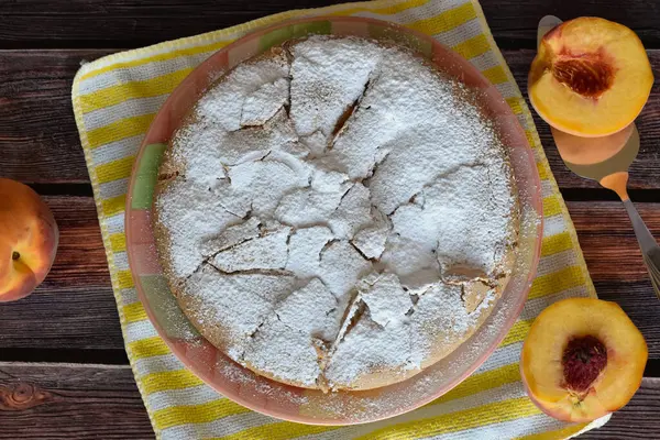 Tahta masada şeftalili ev yapımı Charlotte Pie. Üzerine pudra şekeri serpiştirilmiş kek. Şeftalinin yarısı metal kek küreğinde, sulu şeftali meyvesi, çizgili sarı ve beyaz peçete..