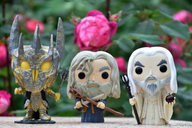 Sauron 'un Funko Pop aksiyon figürleri, Gri Gandalf ve Yüzüklerin Efendisi' ndeki Beyaz Saruman. Gizemli karamsar bahçe, kırmızı güller.
