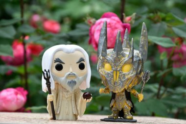 Büyücü Beyaz Saruman 'ın aksiyon figürleri ve Yüzüklerin Efendisi' ndeki Karanlık Lord Sauron. Gizemli karamsar bahçe, kırmızı güller.