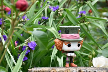 Tim Burton fantezi filmi Alice Harikalar Diyarında 'daki Çılgın Şapkacı' nın aksiyon figürü. Mavi ve beyaz çiçekler, muhteşem bahçe, ahşap kütük.