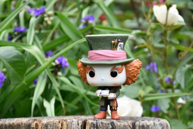 Tim Burton fantezi filmi Alice Harikalar Diyarında 'daki Çılgın Şapkacı' nın aksiyon figürü. Mavi ve beyaz çiçekler, muhteşem bahçe, ahşap kütük.