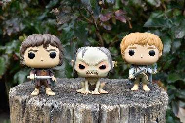 Frodo, Gollum ve Sam 'in fantezi filmi Yüzüklerin Efendisi' ndeki Funko Pop aksiyon figürleri. Karanlık orman, ağaç kütüğü, yeşil yapraklar..