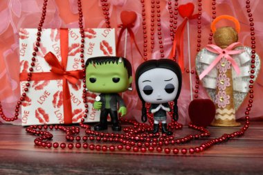 Funko Pop action figures of Frankenstein's monster and Wednesday Addams. Valentine's Day, handmade angel, gift box, necklace, red ribbons, hearts, romance.