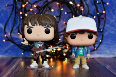 Popüler korku dizisi Stranger Things 'ten Eddie ve Dustin' in Funko Pop aksiyon figürleri. Mavi sisli arka plan, renkli ışıklar, gizemli bir yer..