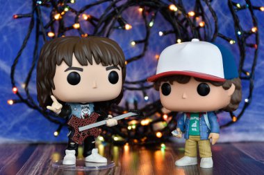 Popüler korku dizisi Stranger Things 'ten Eddie ve Dustin' in Funko Pop aksiyon figürleri. Mavi sisli arka plan, renkli ışıklar, gizemli bir yer..
