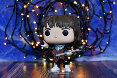 Popüler korku dizisi Stranger Things 'ten Eddie Munson' ın funko pop aksiyon figürü. Mavi sisli arka plan, renkli ışıklar, gizemli bir yer..