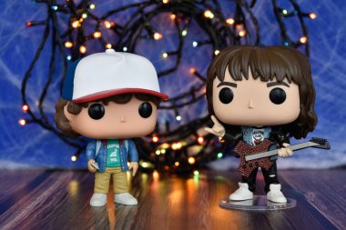 Popüler korku dizisi Stranger Things 'ten Eddie ve Dustin' in Funko Pop aksiyon figürleri. Mavi sisli arka plan, renkli ışıklar, gizemli bir yer..