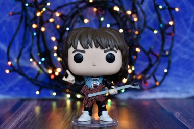 Popüler korku dizisi Stranger Things 'ten Eddie Munson' ın funko pop aksiyon figürü. Mavi sisli arka plan, renkli ışıklar, gizemli bir yer..