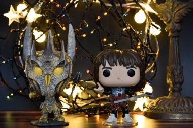 Yüzüklerin Efendisi filminden Funko Pop oyuncakları ve Yabancı Şeyler filminden Eddie. Turuncu ışıklandırma, siyah arkaplan, renkli çelenk, karanlık yer.