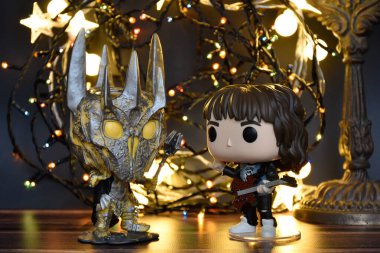 Yüzüklerin Efendisi filminden Funko Pop oyuncakları ve Yabancı Şeyler filminden Eddie. Turuncu ışıklandırma, siyah arkaplan, renkli çelenk, karanlık yer.