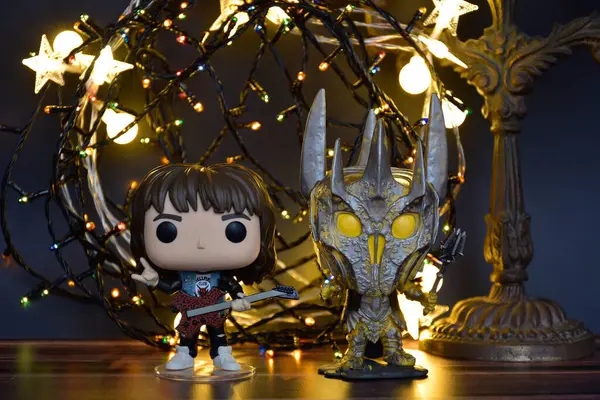 Yüzüklerin Efendisi filminden Funko Pop oyuncakları ve Yabancı Şeyler filminden Eddie. Turuncu ışıklandırma, siyah arkaplan, renkli çelenk, karanlık yer.